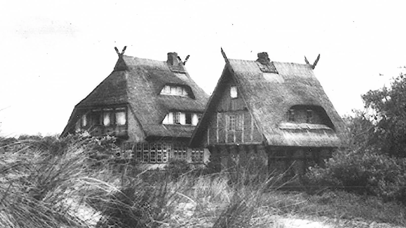 Historische Schwarz-Weiß-Aufnahme: Haus Windhook mit zwei Reetdachgiebeln, eingebettet ins Dünengras